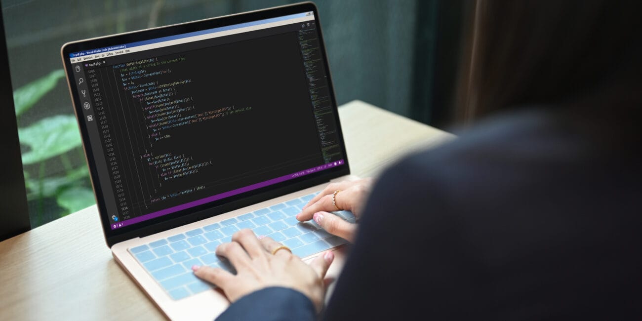 Over shoulder view of female software developer working on web site project, programming on desktop computer in startup company.