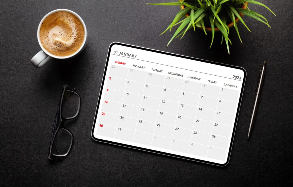 A tablet displaying a monthly calendar next to a coffee cup and plant — symbolizing automation and time management.