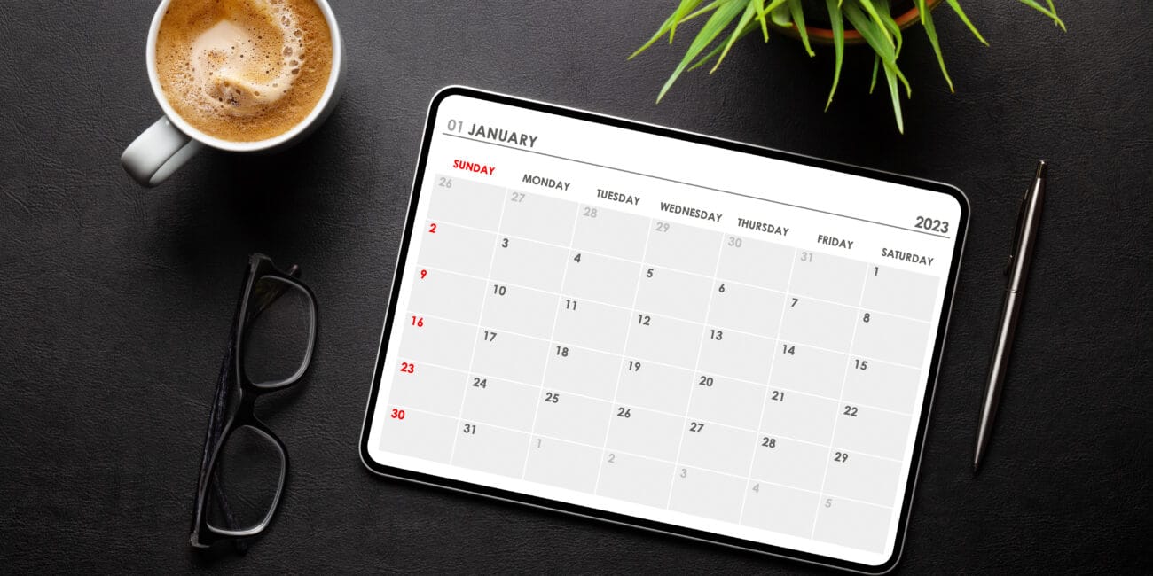 Tablet with calendar app, coffee cup and office supplies on desk. Top view flat lay